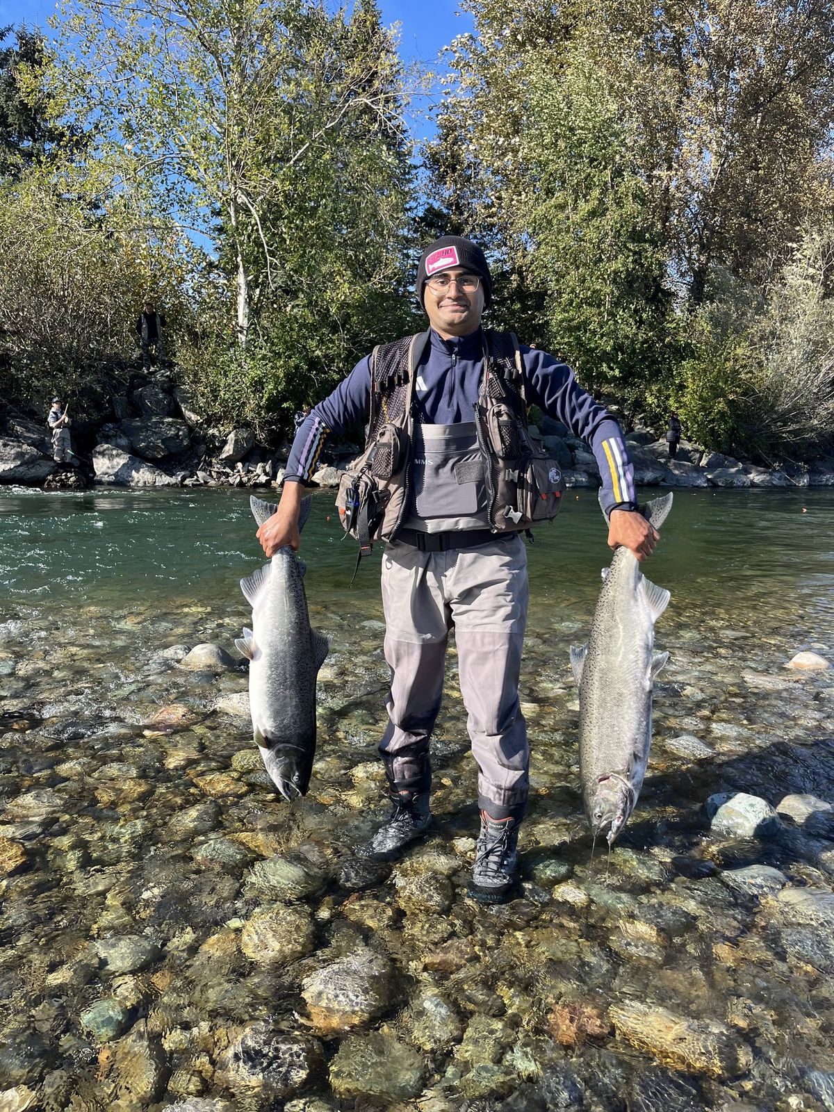 Aneesh holding two salmon, one in each hand, in a BC river